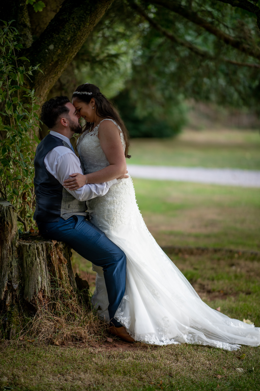 Couple sharing a quiet moment with groom sat on a tree stump under large trees
