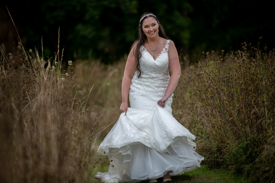 Smiling bride walking along a grass pathway among an Autumn wid flower meadow