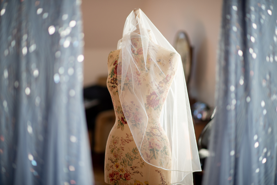 Bridal veil draped over dressmakers dummy between two sparkling bridesmaids dresses.