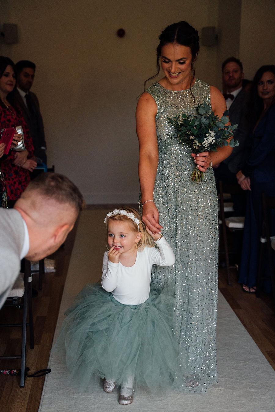 Adorable bridesmaid wearing a tutu walking down the aisle holding her mums hand.