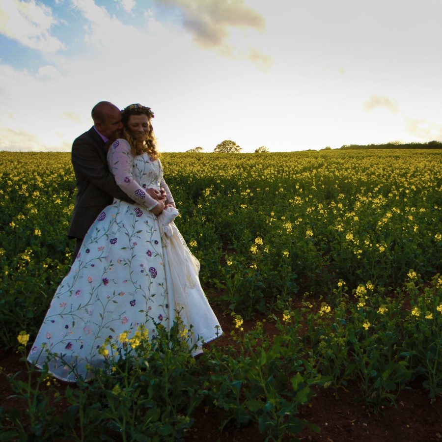Bride and groom standing in a field of rape in the evening sun.
