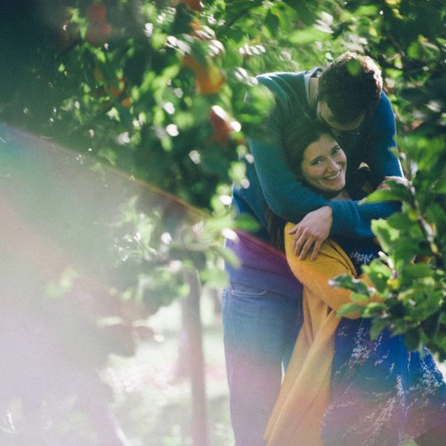 Newly engaged couple embracing in an orchard.