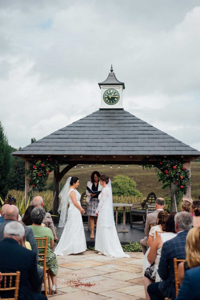 Two brides under the clock tower at Harefield Barn wedding venue Devon