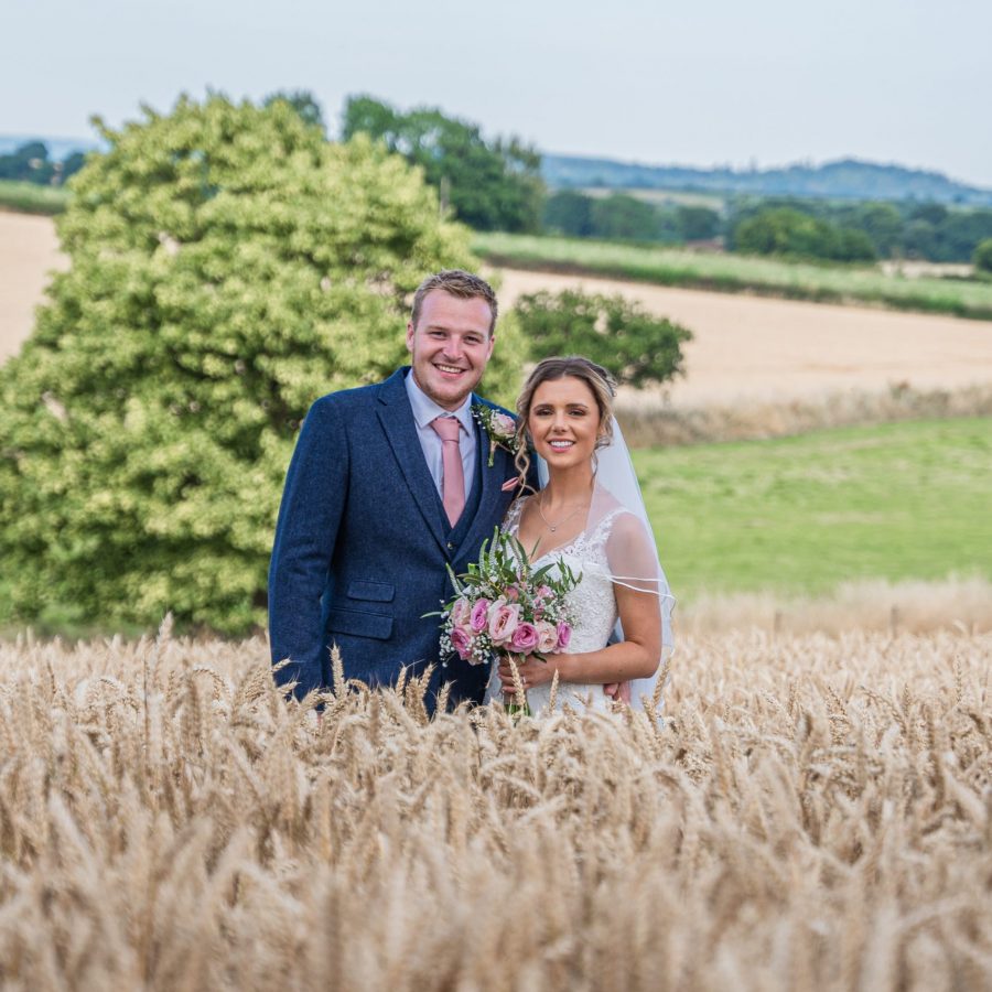 Bride and Groom standing in a ripe corn field with views behind.